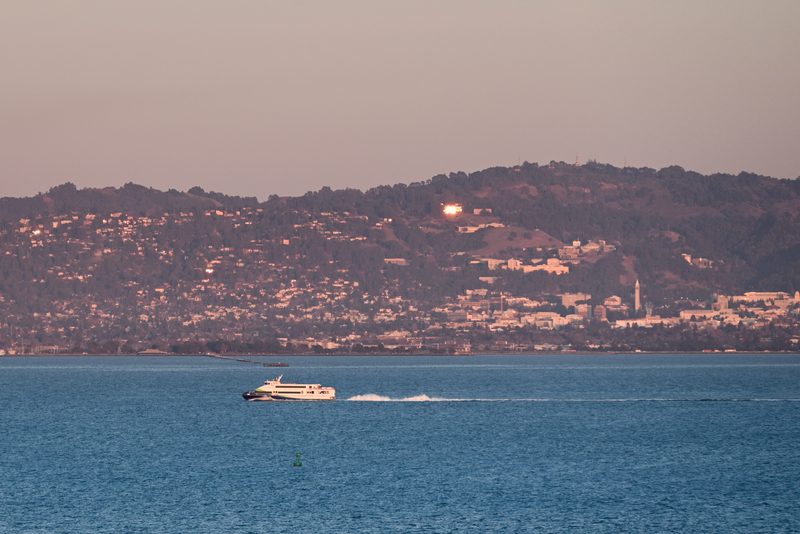 Hillside city across the bay at dusk, a small boat crossing