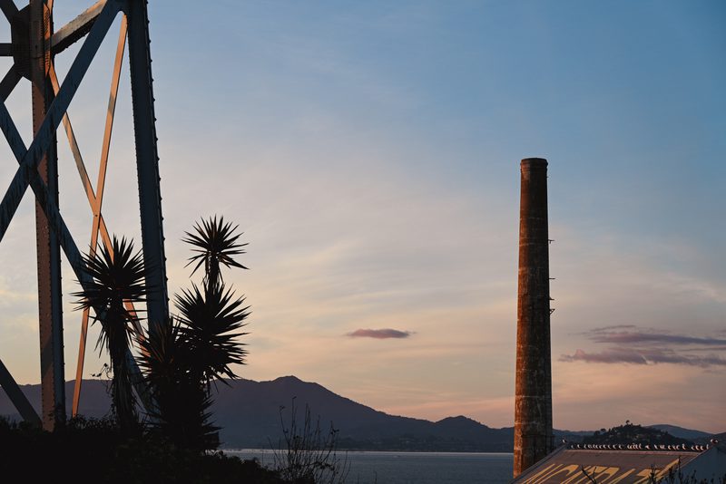 Rusted water tower and brick chimney against a sunset sky