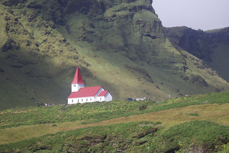 White church with a red roof on a green hillside