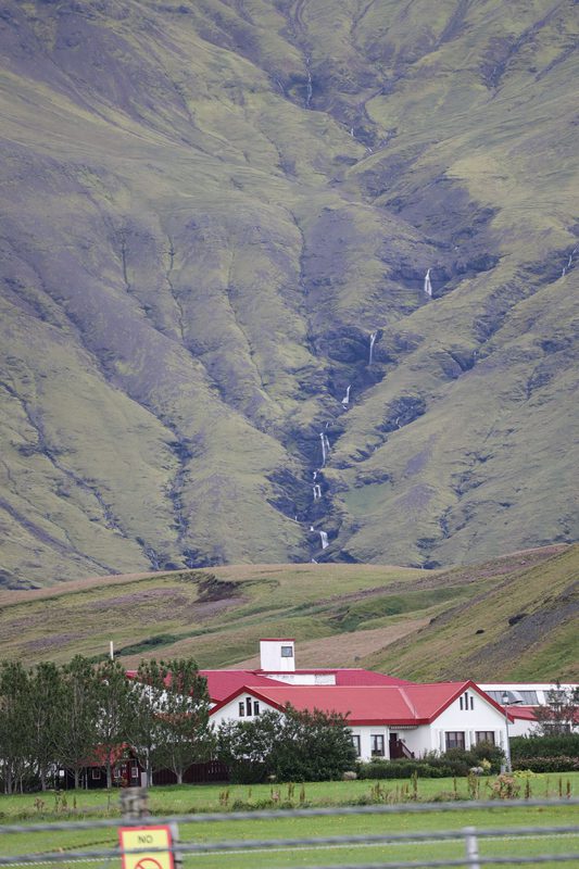 Thin waterfalls streaking down a mountainside behind red-roofed houses
