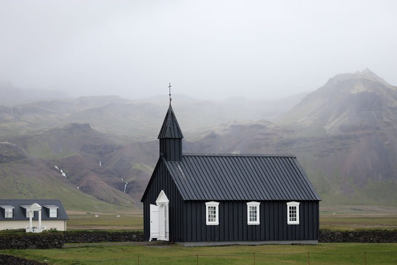 Black wooden church with white windows below misty mountains