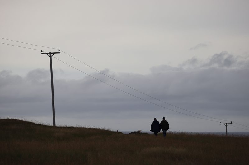 Two figures walking under a power line beneath a heavy grey sky